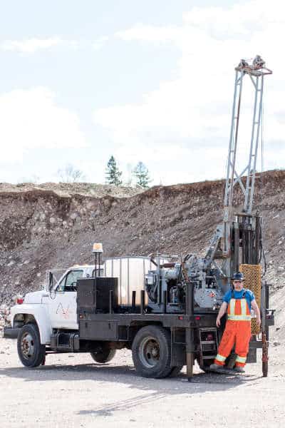 Operator standing beside truck mounted drilling rig in an Ontario quarry